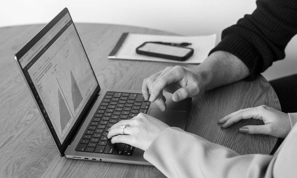 Two business co-founders collaborating on a laptop, discussing a cybersecurity marketing plan.
